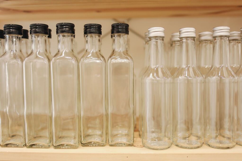 Glass bottles and jars displayed beside plastic bottles and containers to compare sustainable packaging materials.